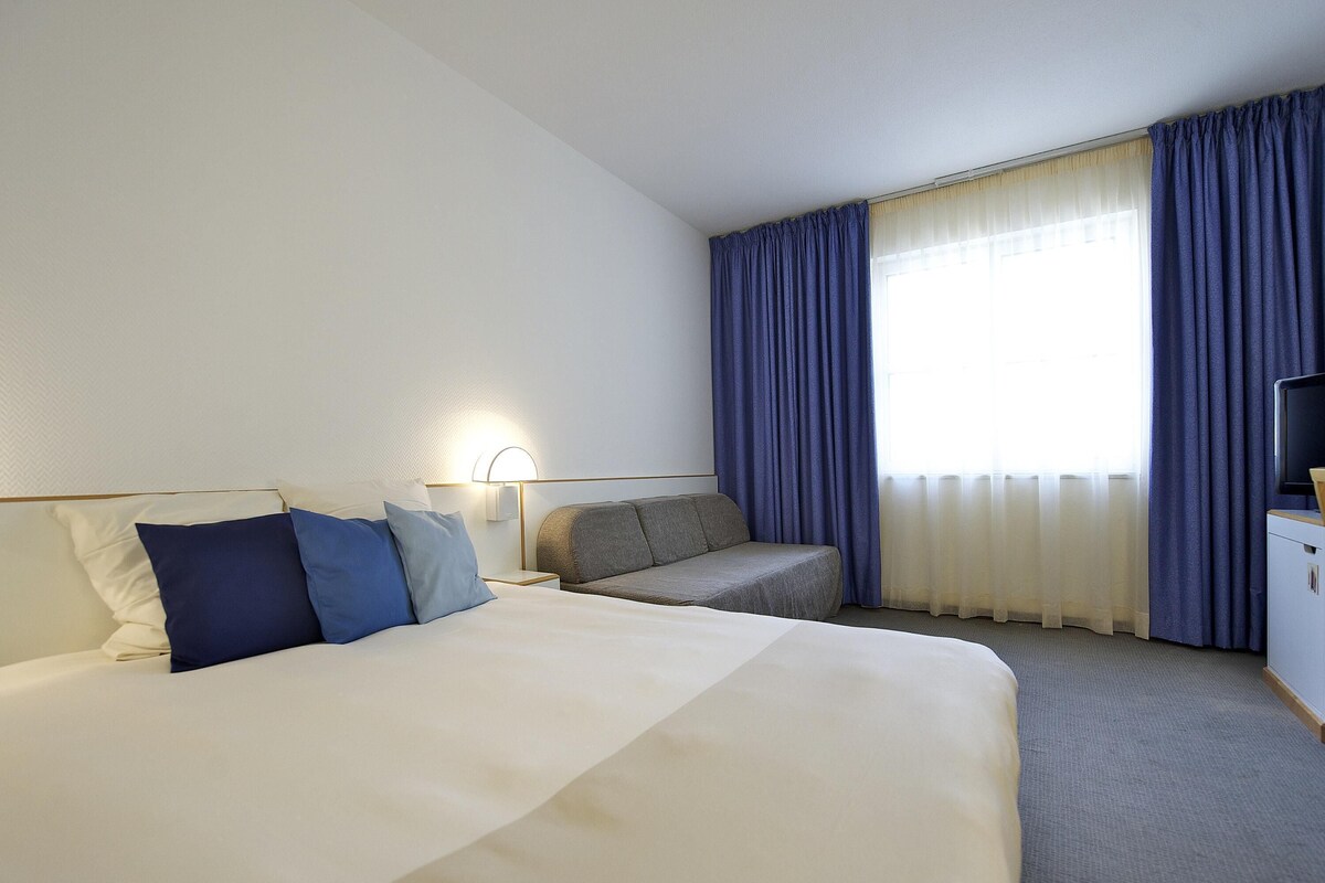 A hotel room with a large bed, a sofa, a desk, and a television.