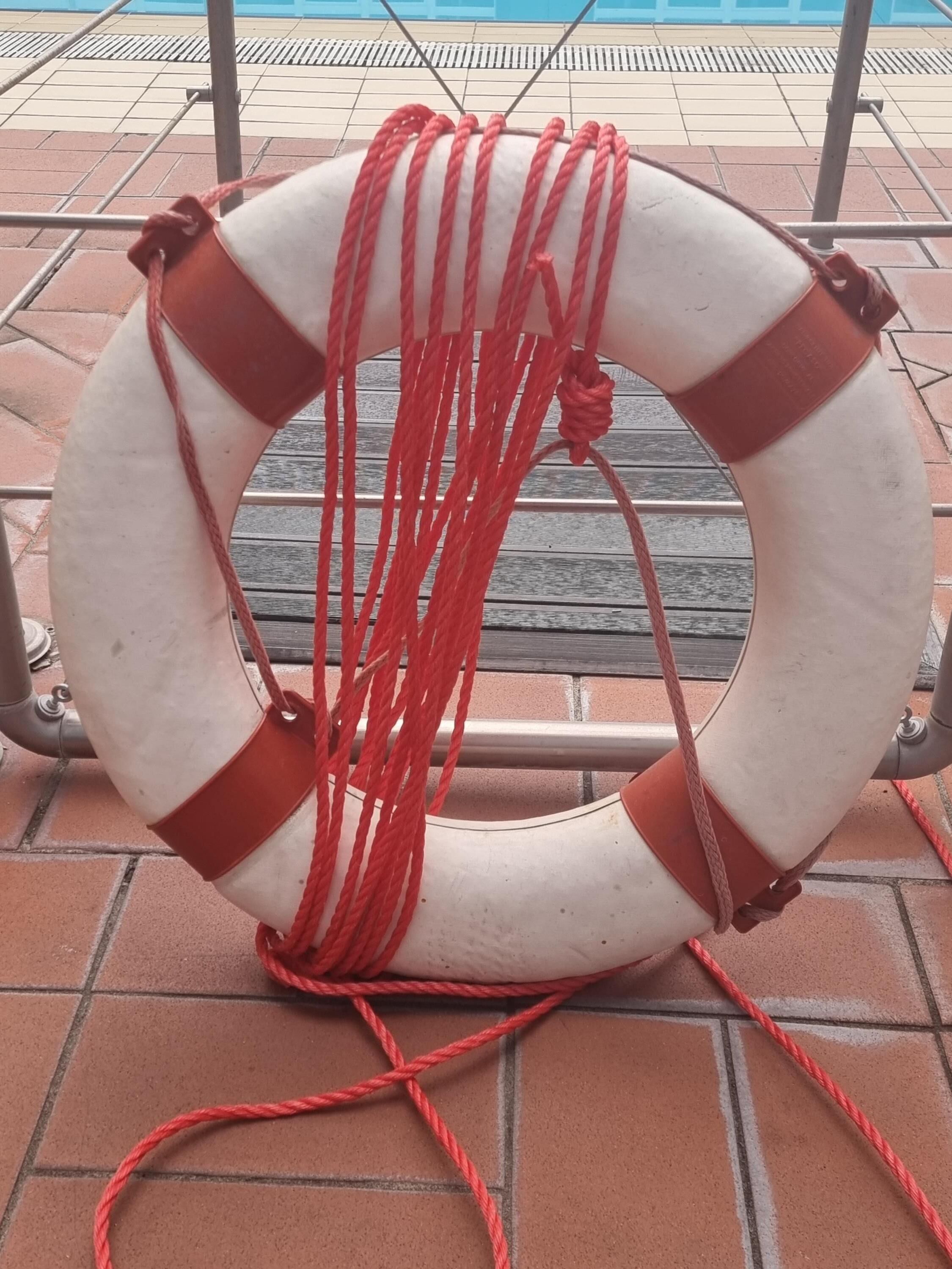 Een drijvend reddingsmiddel met rode touwen, geplaatst op een betegeld oppervlak nabij een zwembad.