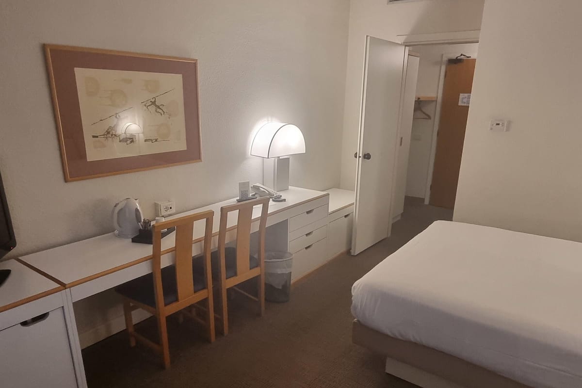A hotel room with a bed, a desk with a chair, a lamp, and a framed picture on the wall.