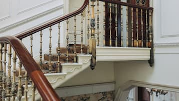 A grand staircase with ornate balustrades and a chandelier, leading to a balcony with a stained glass window.