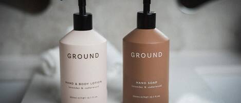 Dos botellas de loción de manos y jabón hechos a mano, con dosificadores negros, etiquetadas con aroma a lavanda y cedro, sobre una superficie de mármol.
