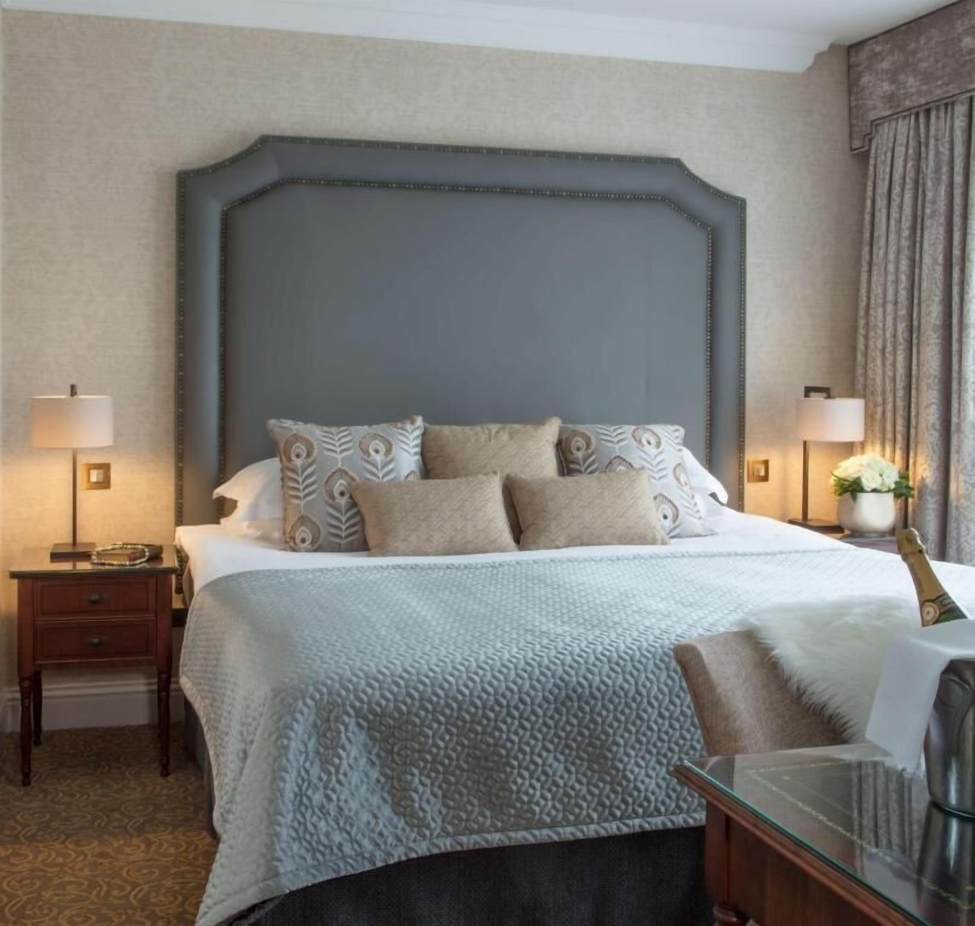 Una habitación de hotel ordenada con una cama grande, dos mesitas de noche y un buró.