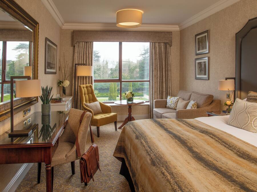 A hotel room with a large bed, a sofa, a chair, a desk, and a large window offering a view of the outdoors.