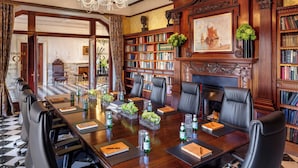 Un salón de reuniones formal con una gran mesa de madera, sillas de cuero, estanterías y un candelabro.