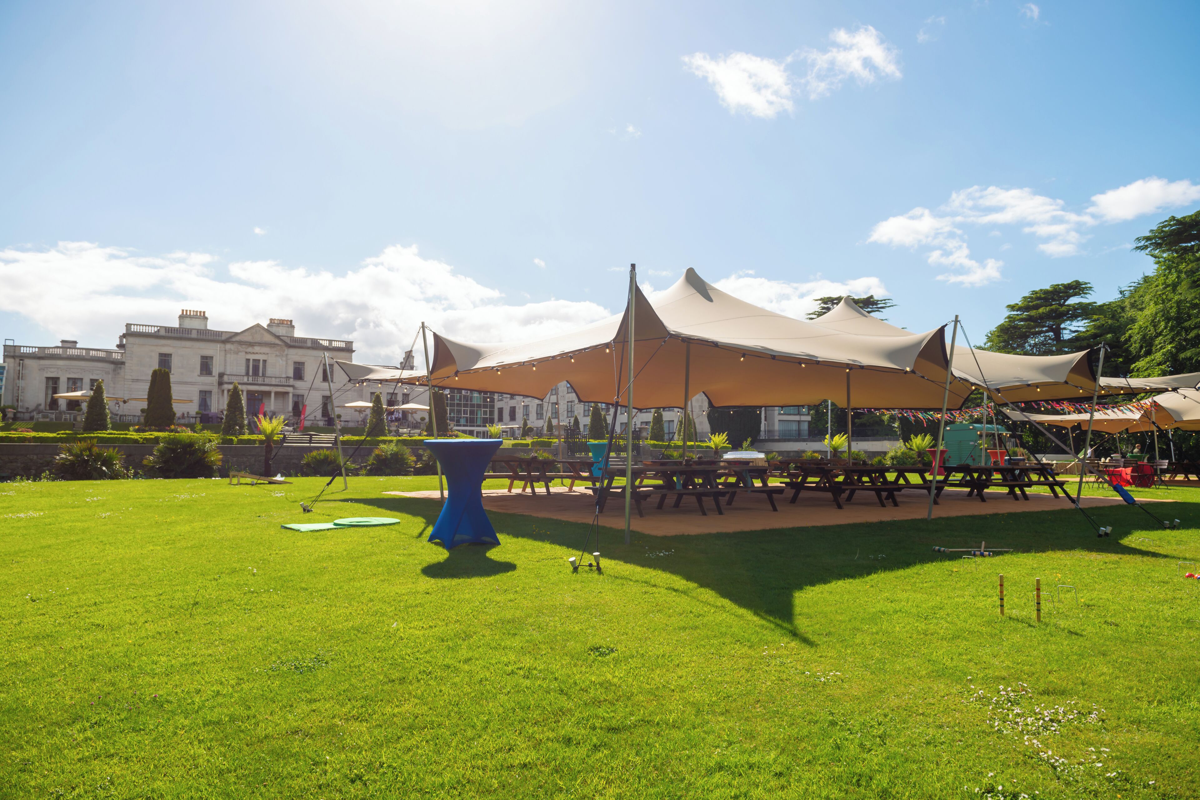 A grassy outdoor area with picnic tables and a blue table.