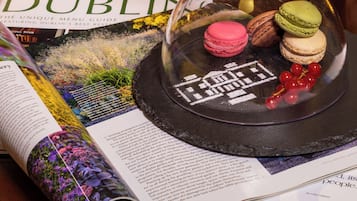 A dining menu, a glass dome with macarons, and a wooden box with white spheres on a table.