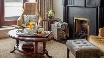 A cozy room with a fireplace, a round wooden table with breakfast items, a comfortable armchair, and a cushioned bench.