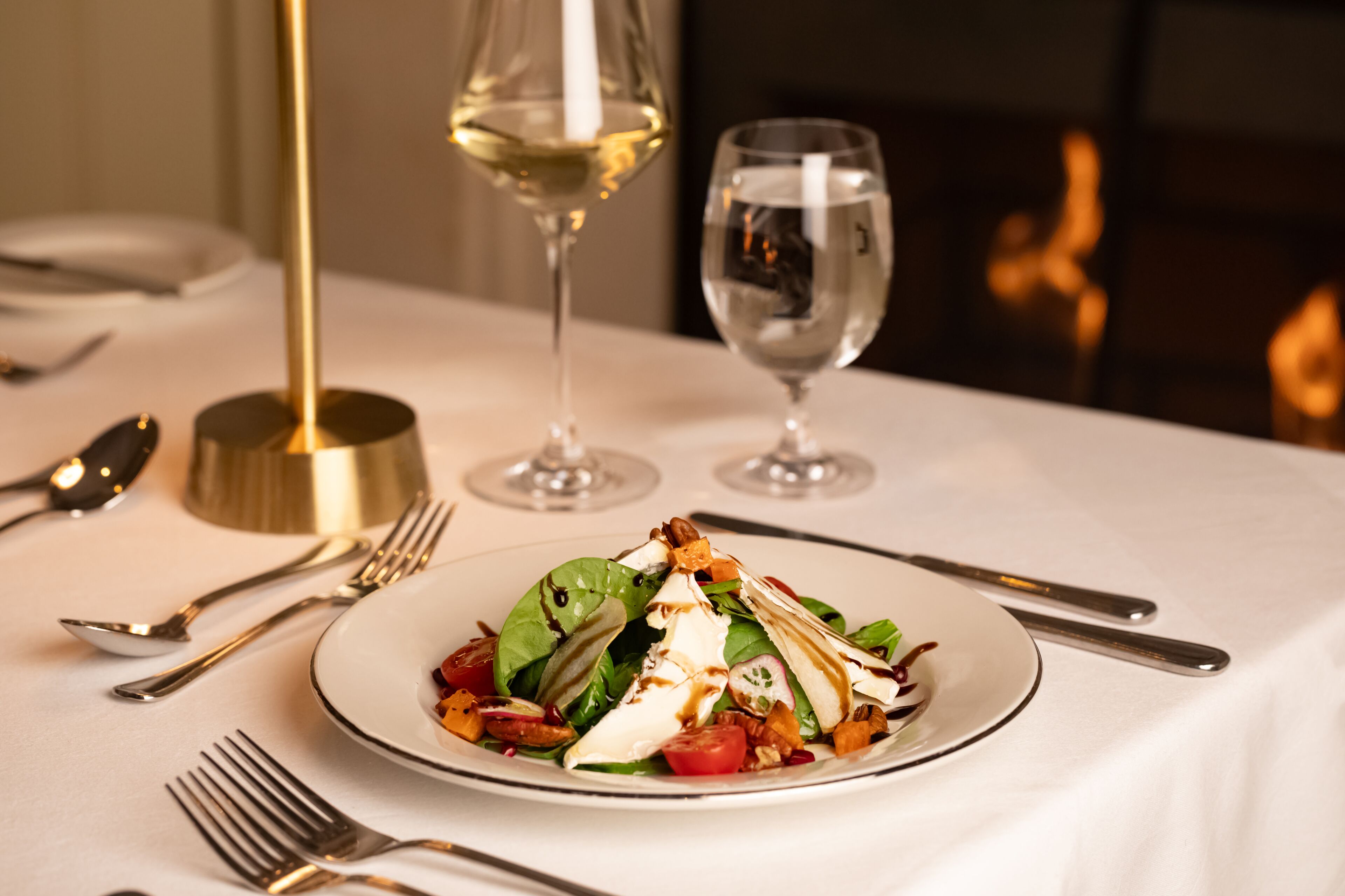 A dining table with a plate of salad, wine glasses, and cutlery.