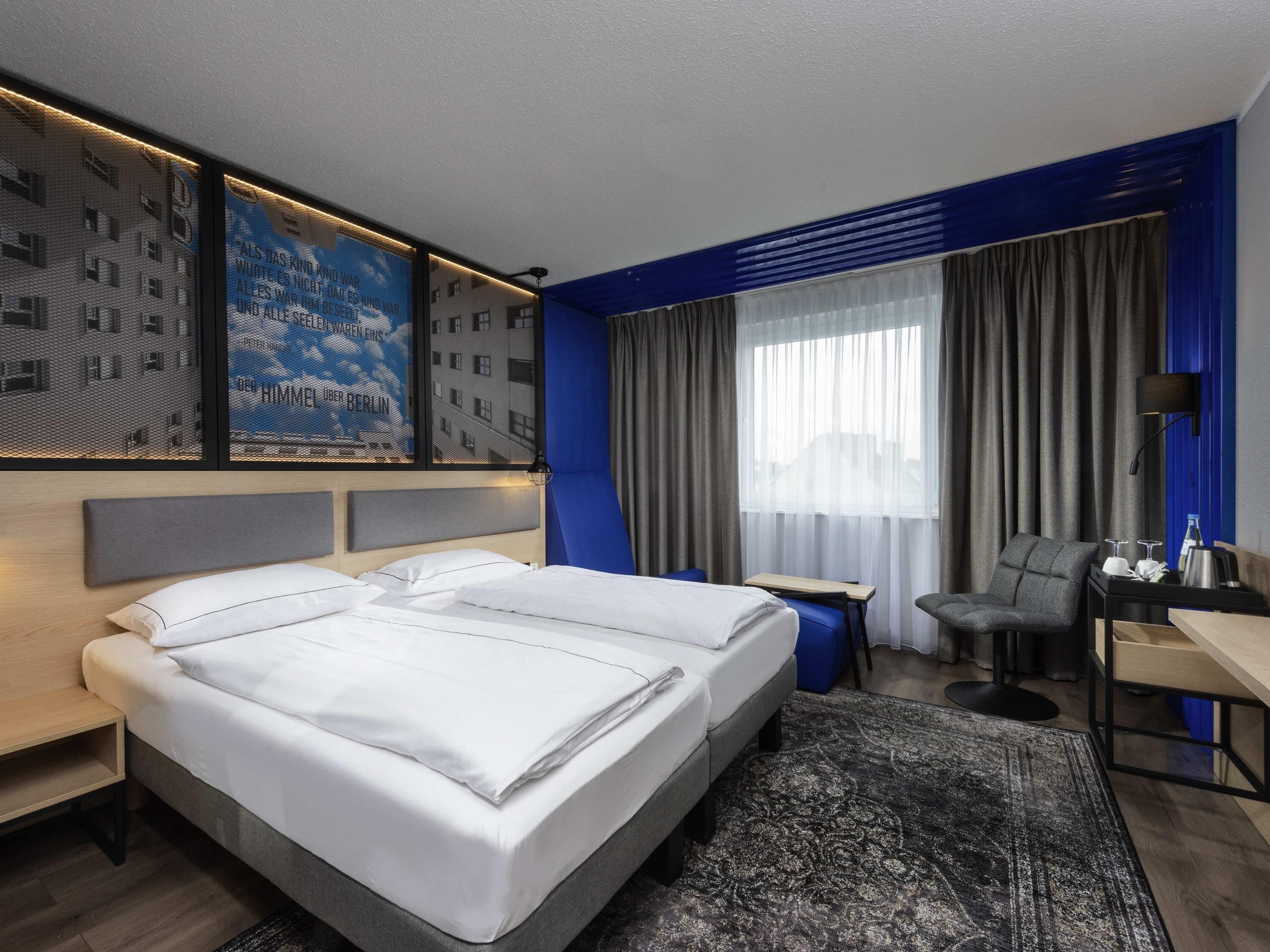 A modern hotel room with a large bed, a desk, a chair, and a view of the city.