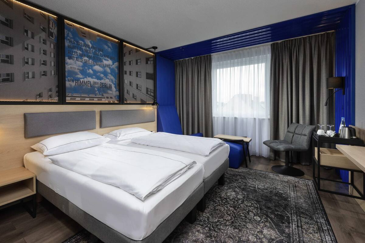 Ein modernes Hotelzimmer mit einem großen Bett, einem Schreibtisch, einem Sessel und Blick auf die Stadt.