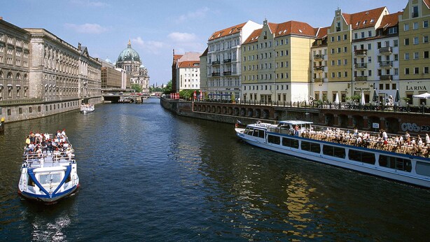 A river with a boat carrying passengers, surrounded by historic buildings with varied architecture. - ibis Styles Berlin Treptow (Berlin)