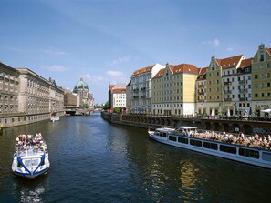 A river with a boat carrying passengers, surrounded by historic buildings with varied architecture. - ibis Styles Berlin Treptow (Berlin)