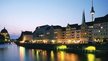 Blick auf eine Stadt am Flussufer mit historischen Gebäuden, einem markanten Turm und einer Brücke.