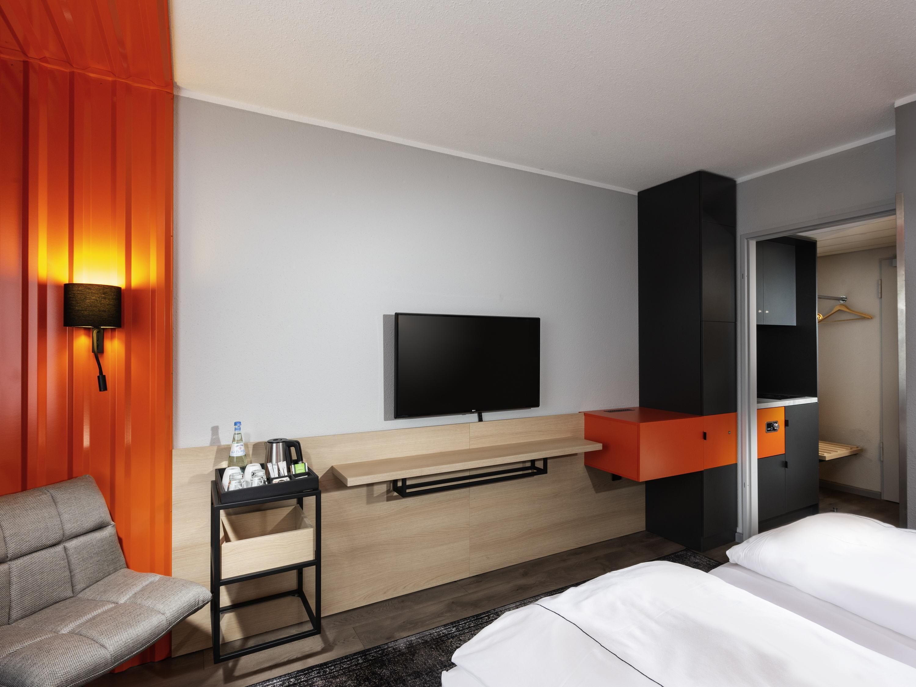A hotel room with a bed, a TV, a desk with a chair, and a wardrobe.