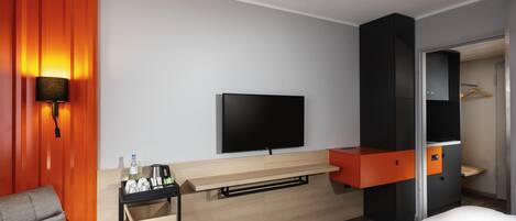 A hotel room with a bed, a TV, a desk with a chair, and a wardrobe.