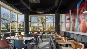A restaurant interior with large windows, modern furniture, and a mural on the wall. - ibis Styles Berlin Treptow (Berlin)