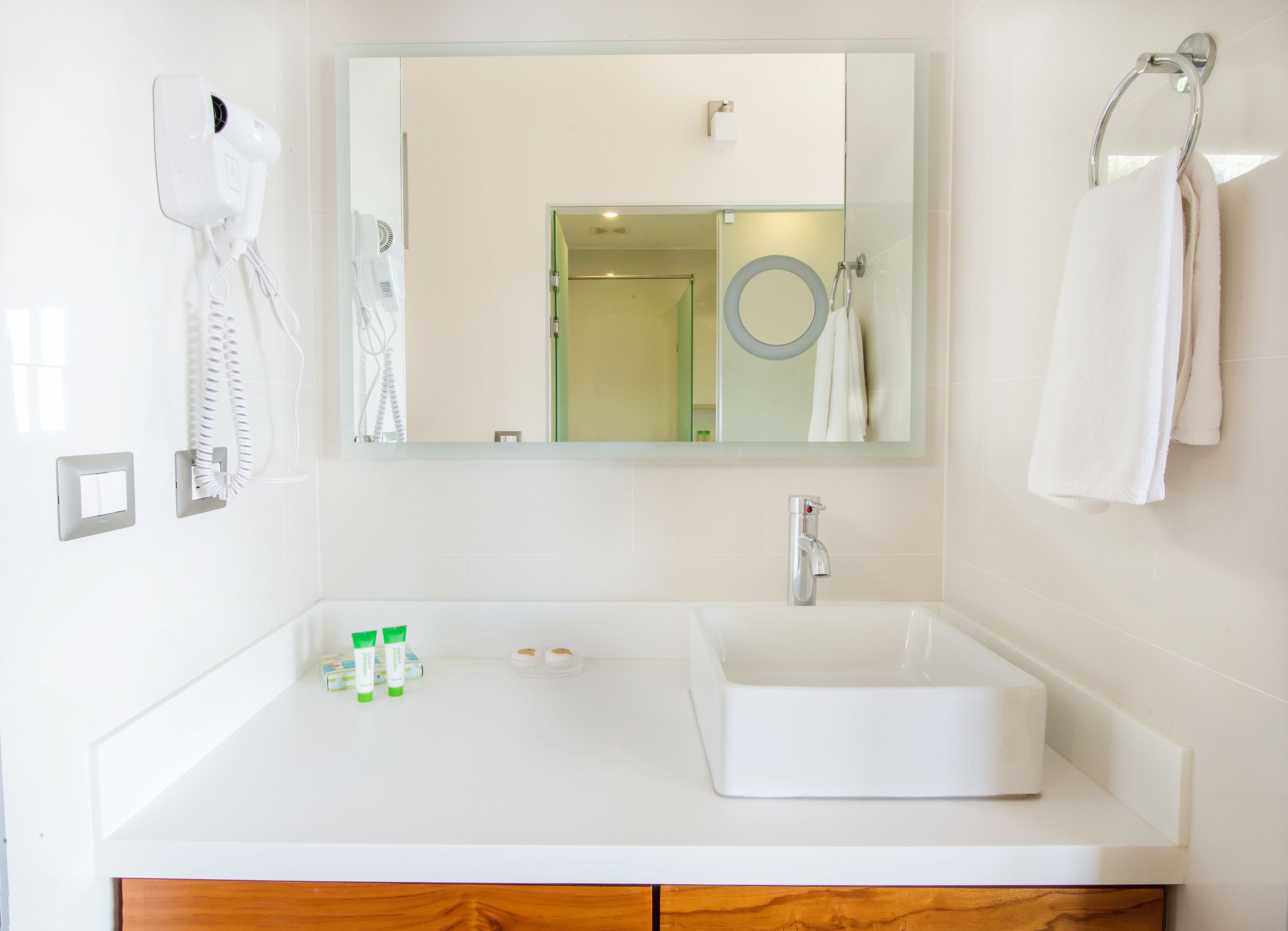 A modern bathroom with a white sink, a mirror, a towel ring, and a hairdryer on the wall.