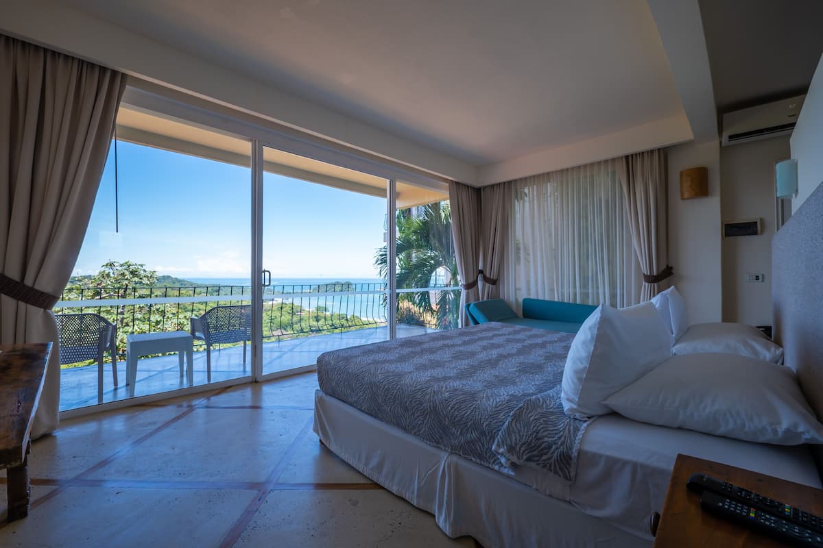 Une chambre d’hôtel avec un grand lit, un balcon donnant sur la mer et une table avec une télécommande.