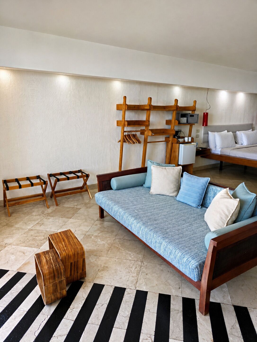 A modern living room with a sofa, wooden benches, a coffee table, and a bed with white bedding.