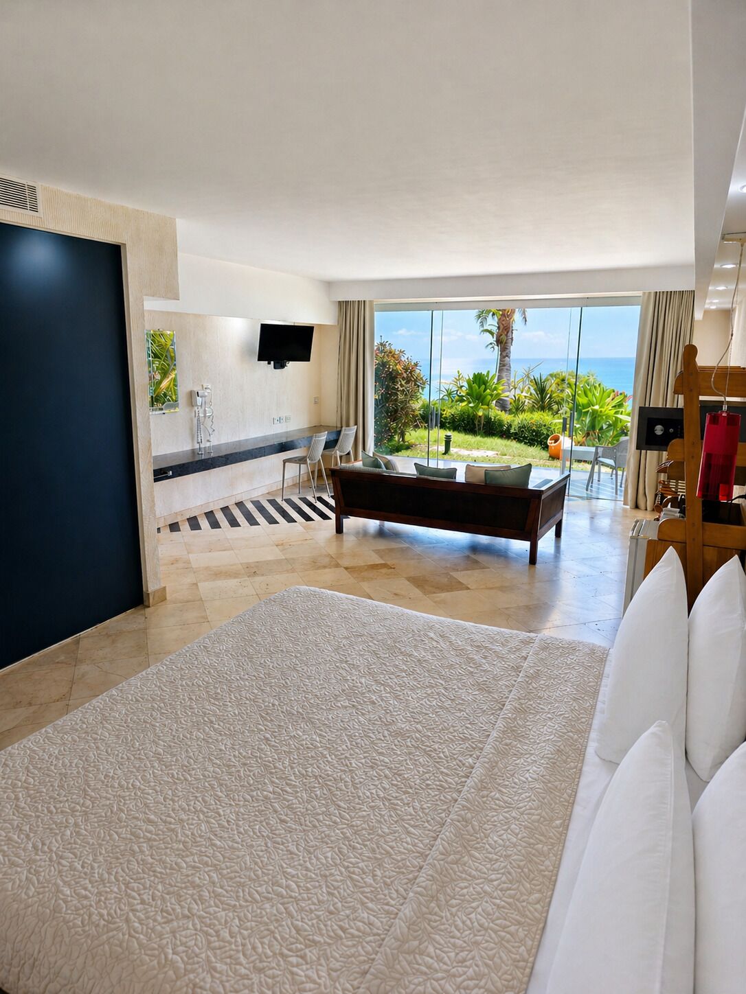 Una camera d'albergo moderna con un letto grande, una poltrona, una TV e un balcone vista oceano.