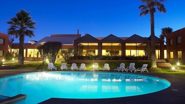 Ein Swimmingpool mit Liegestühlen, Palmen und einem Gebäude mit überdachter Terrasse.