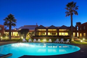 A swimming pool with lounge chairs, palm trees, and a building with a covered patio area. - Park Hotel Calama (Calama)