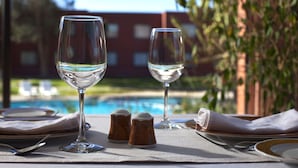 Ein Tisch für zwei Personen gedeckt mit Weingläsern, Salz- und Pfefferstreuern und einer Servette. Im Hintergrund ist ein Schwimmbecken zu sehen.