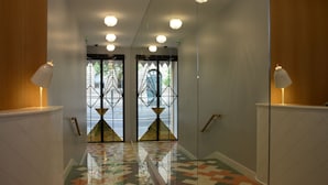 A hallway with a checkered floor, mirrored walls, and a pair of doors with geometric glass patterns. - Le Lapin Blanc (Paris)