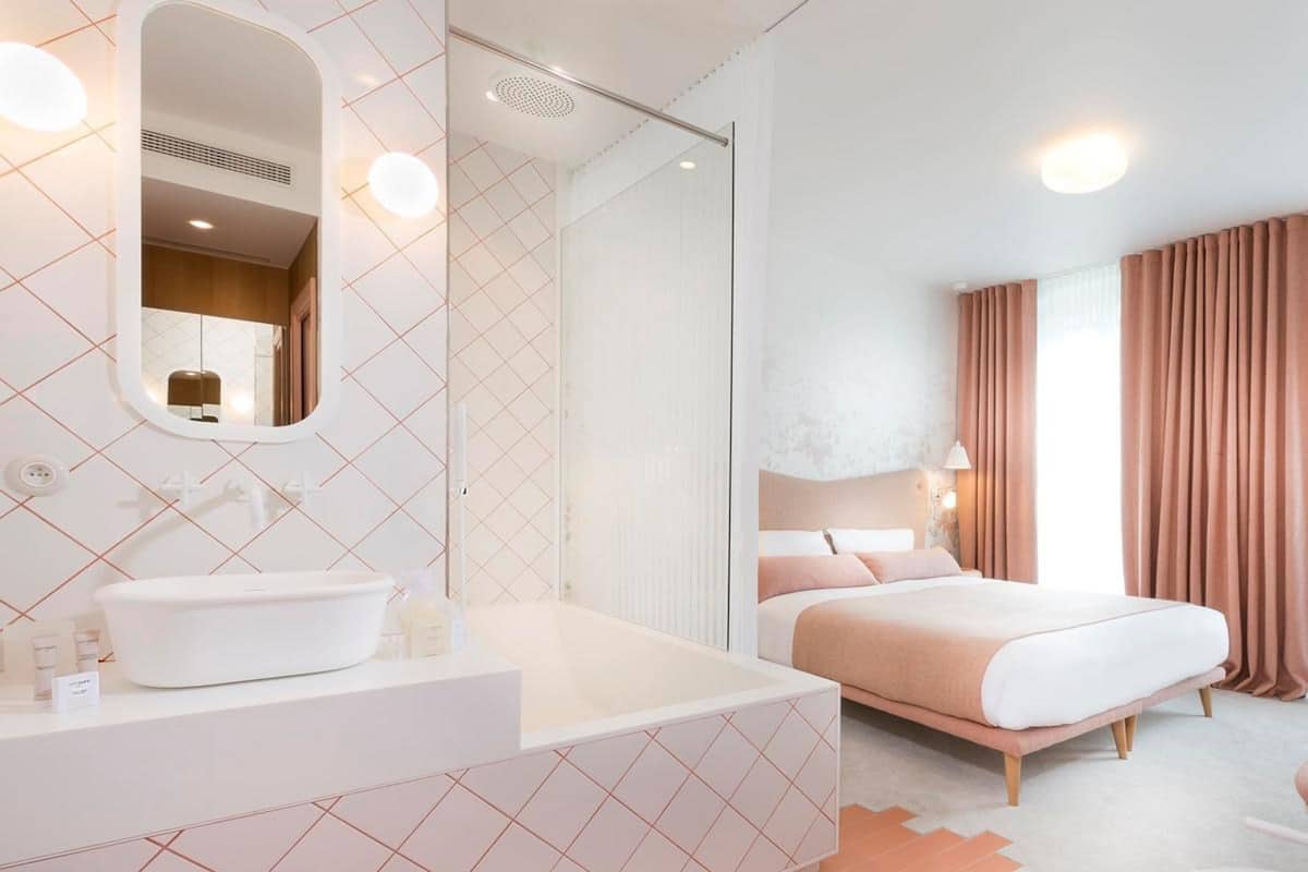 A modern hotel room with a large bed, a separate bathroom with a white sink, and a large mirror.