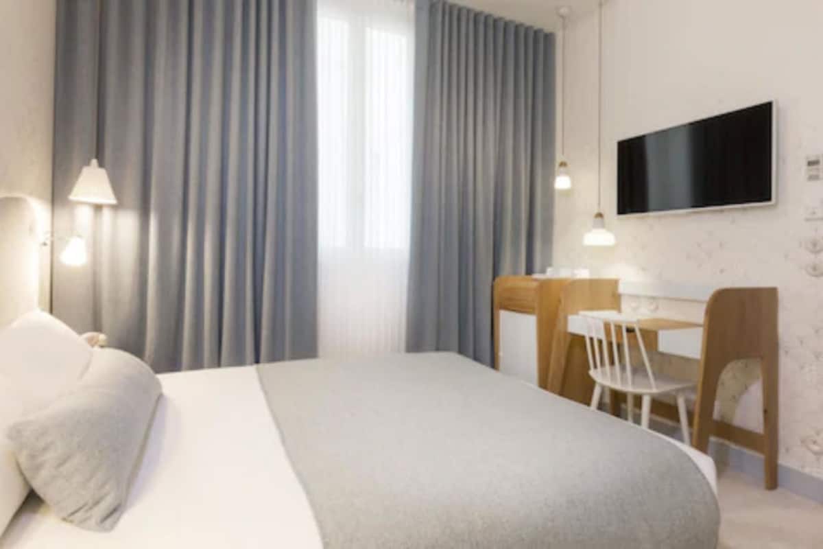 A hotel room with a bed, a desk, a chair, a TV, and curtains.
