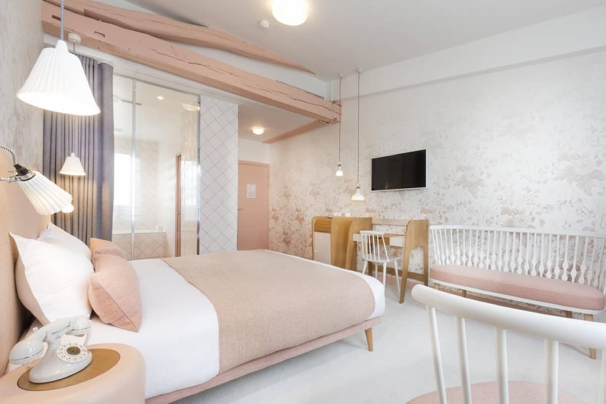 A bedroom with a bed, bedside table with a telephone, a desk, and a chair.