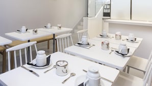 A modern dining area with white tables and chairs, equipped with tea sets and cutlery. - Le Lapin Blanc (Paris)