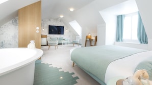 A modern bedroom with a large bed, a sitting area with chairs, a desk, and a TV. - Le Lapin Blanc (Paris)