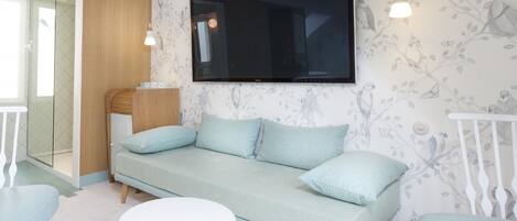 A modern living room with a light blue sofa, a flat-screen TV, and a white round table.