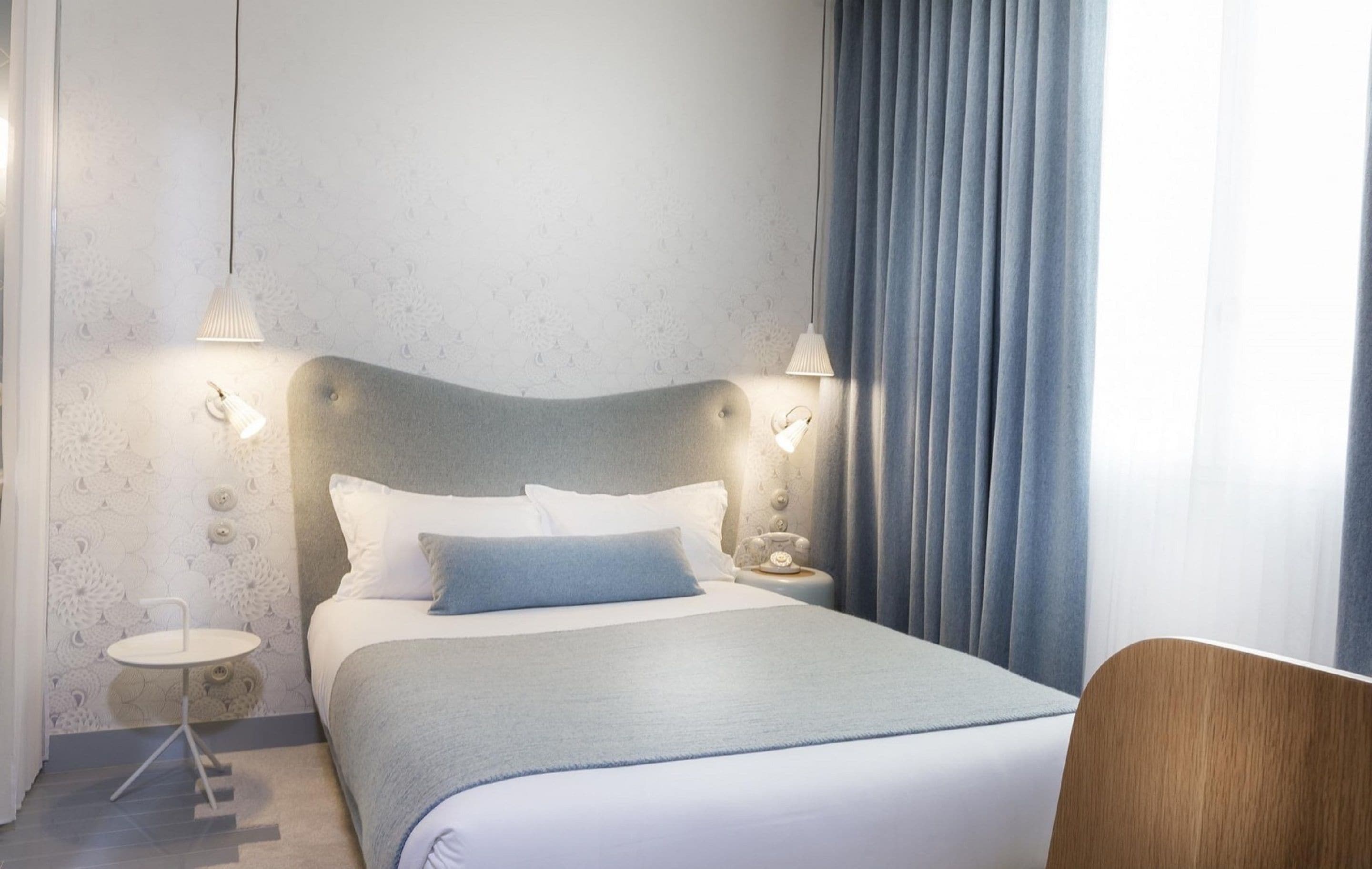 Siististi järjestetty hotellihuone, jossa on sänky, yöpöydät ja tuoli.