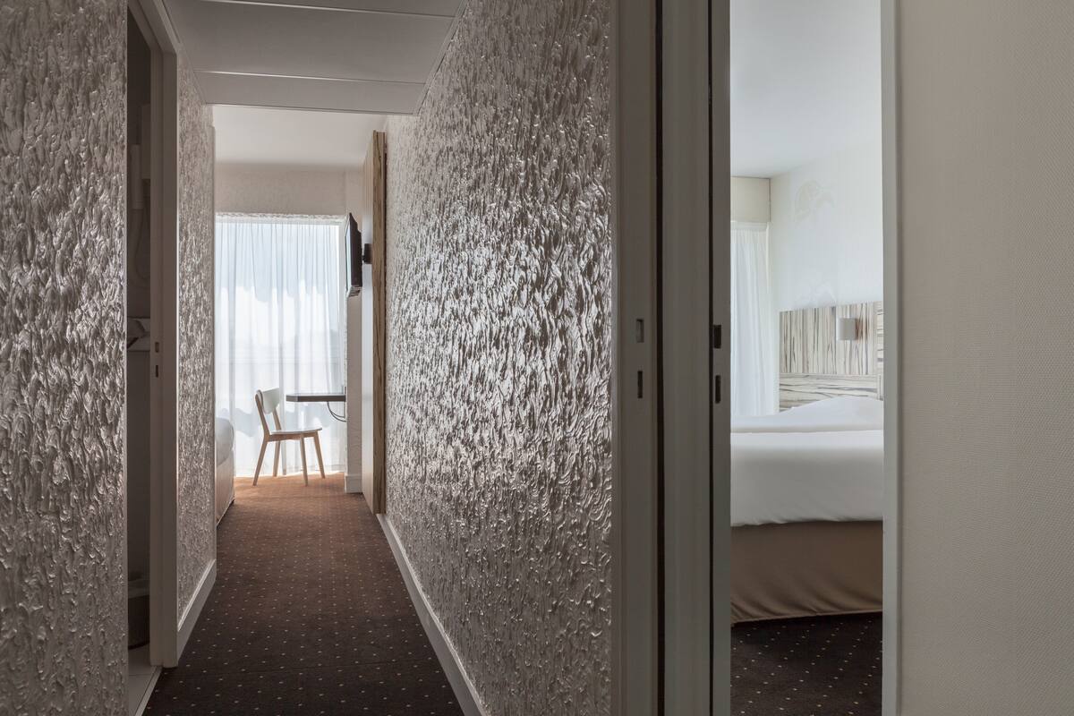 A hotel hallway with textured walls, a bed, and a desk with a chair.