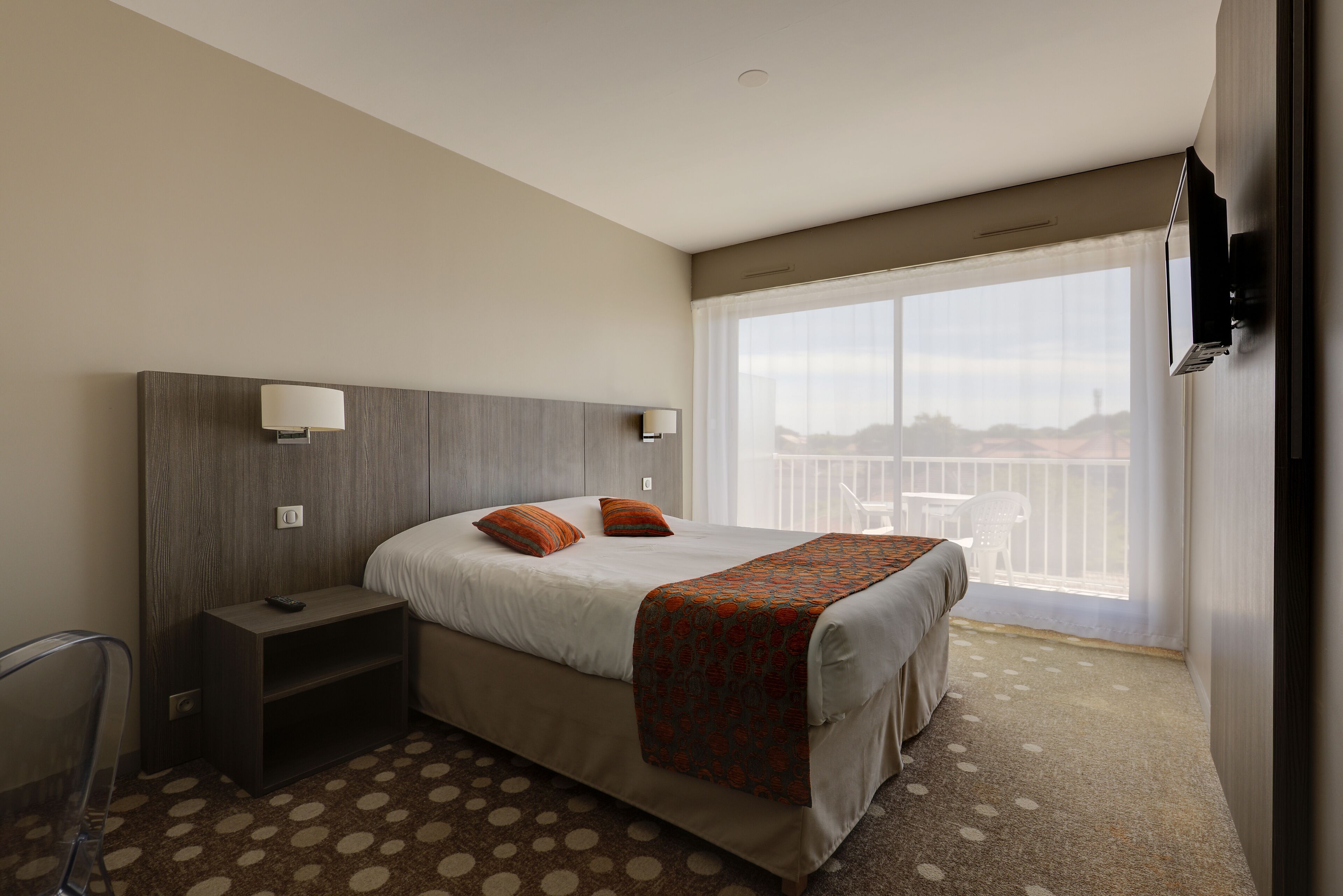A hotel room with a bed, a nightstand, a TV, and a balcony with a view.