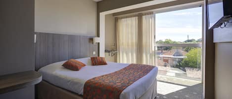 Habitación de hotel con una cama grande, una mesita de noche, una ventana con cortinas y vistas a edificios.