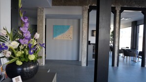 Uma área de recepção moderna com um grande arranjo de flores, uma pintura minimalista e uma área de estar ampla com mesas e cadeiras.