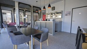 Um interior moderno com uma mesa central e cadeiras, área de bar e um relógio visível na parede.