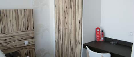 Un dormitorio con una cama, un armario de madera, un escritorio con una silla y una mesita con una caja roja.