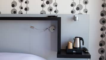 A modern hotel room with a bed, a bedside table with a kettle, a phone, and a small lamp.