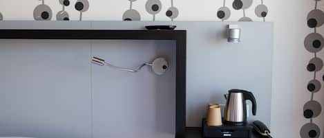 A modern hotel room with a bed, a bedside table with a kettle, a phone, and a small lamp.