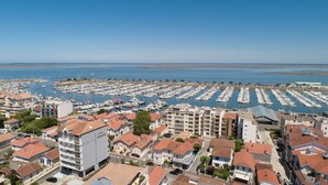 Uma marina com vários barcos atracados em formação circular, rodeada por edifícios residenciais com telhados de telha vermelha.