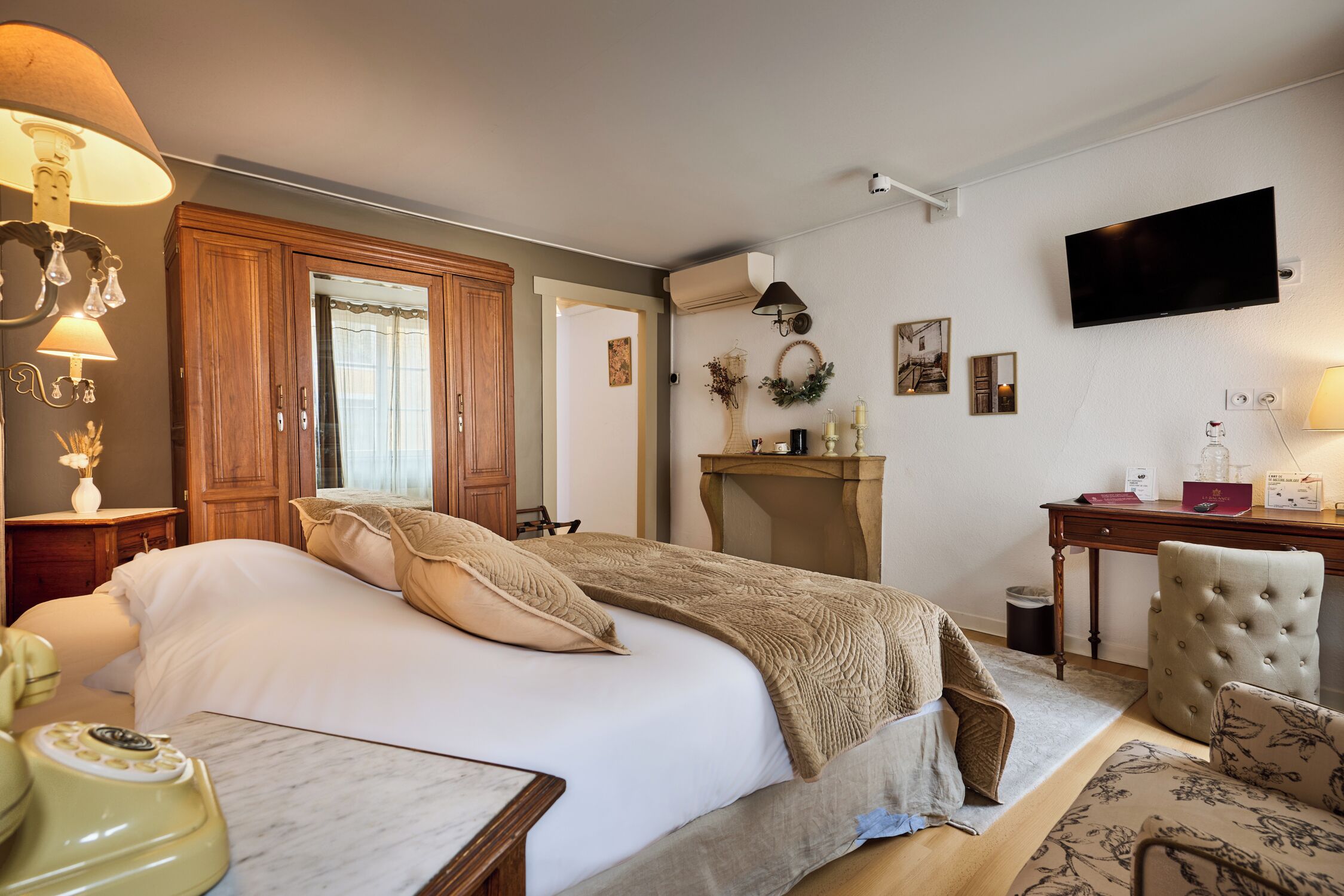 A bedroom with a large bed, wooden wardrobe, bedside table with lamp, and a television mounted on the wall.