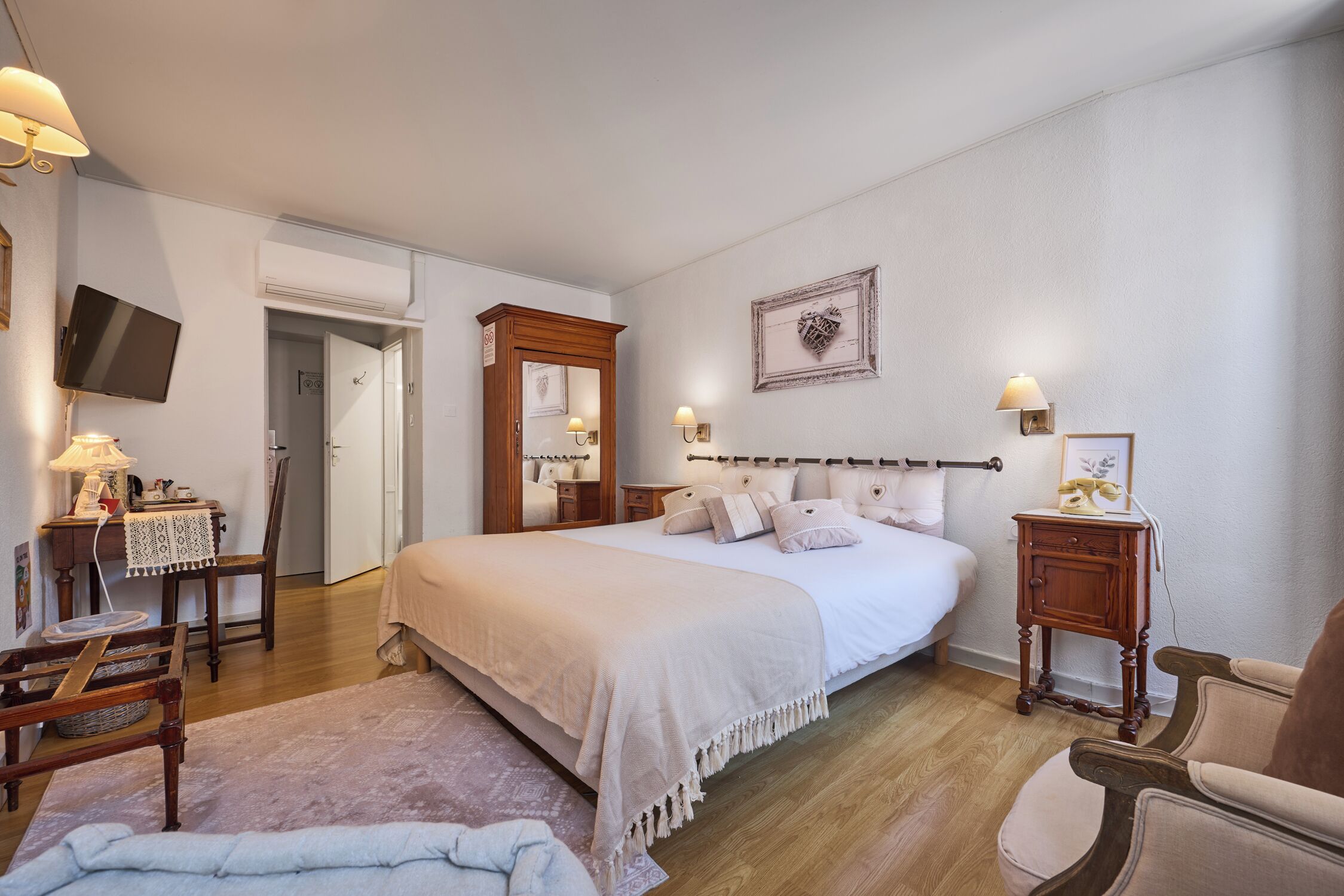A bedroom with a large bed, bedside tables, a chair, a desk, a television, and a mirror.