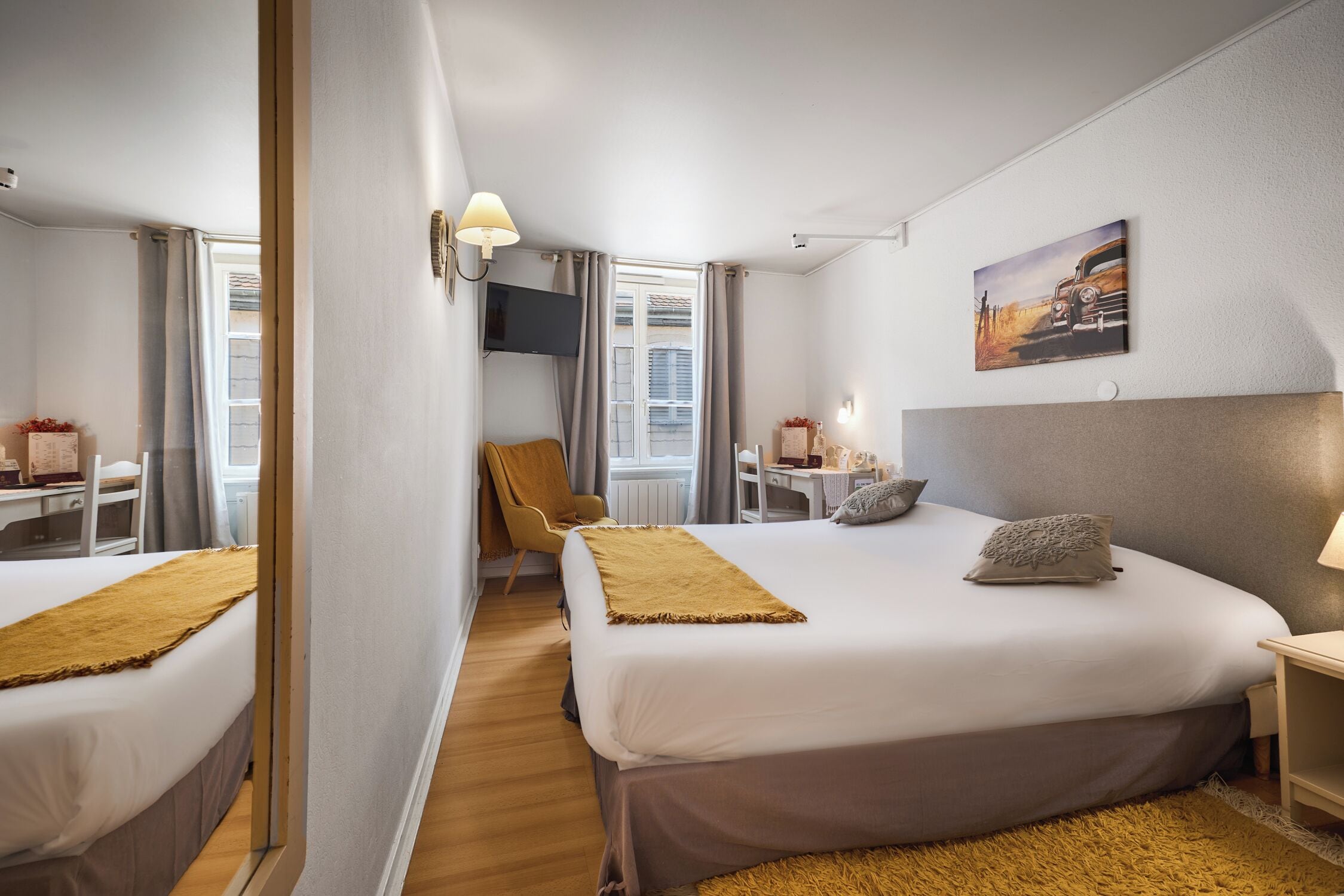 Hotellihuone, jossa on kaksi sänkyä, työpöytä, tuoli, televisio ja taulu seinällä.