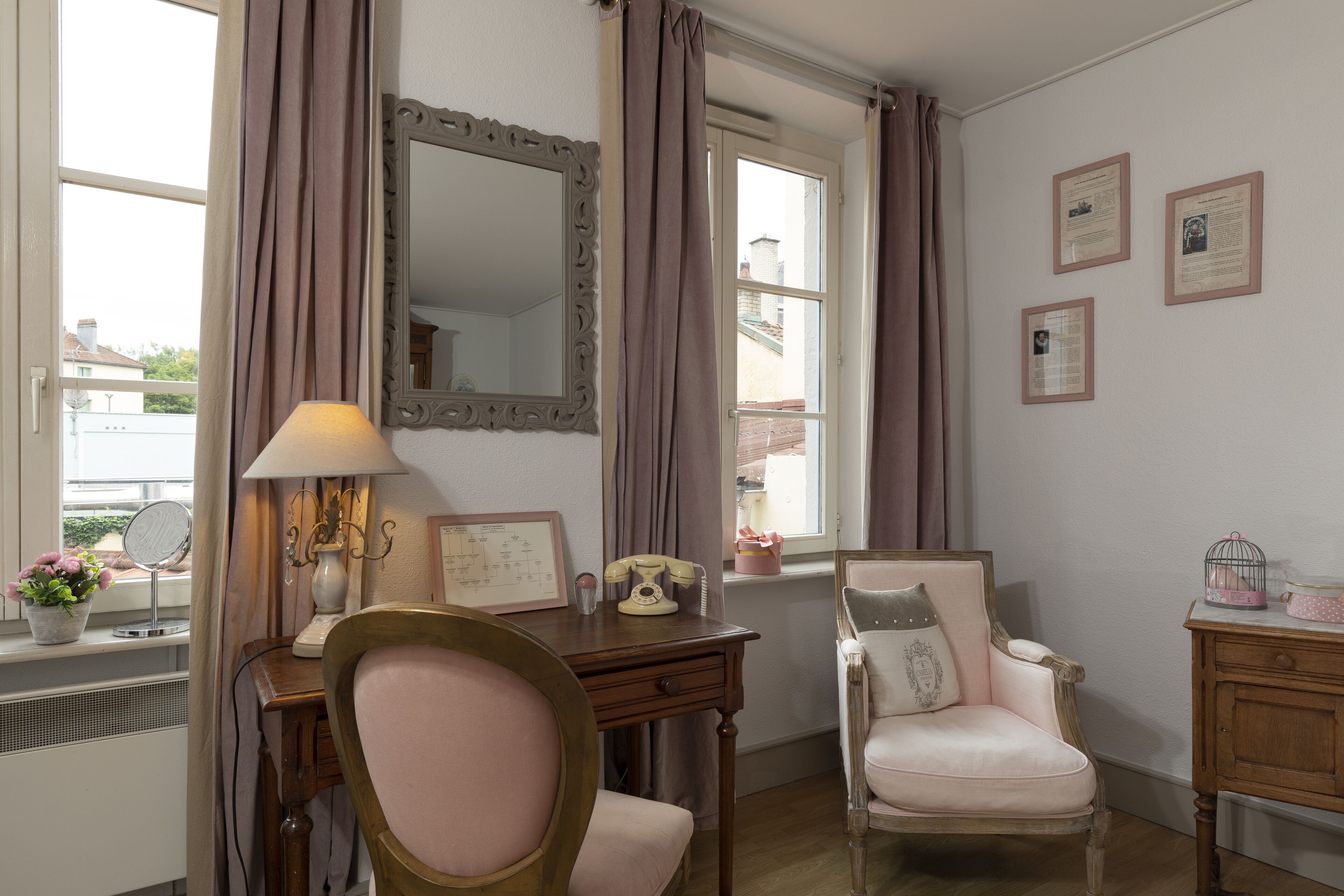 Habitació amb escriptori, cadira i un mirall gran. Hi ha cortines a les finestres i una làmpada sobre l'escriptori.