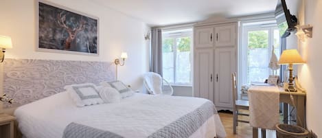 A bedroom with a large bed, a desk, a chair, and a television.
