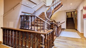 Una amplia escalera con balaustres de madera y barandilla de cristal, que conduce a un piso superior.